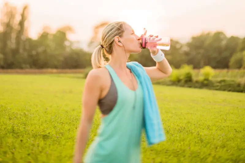 Femme qui boit de l’eau après le sport dans un parc