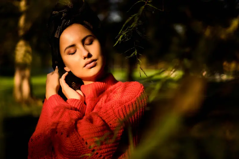 Femme au pull rouge, les yeux fermés au soleil