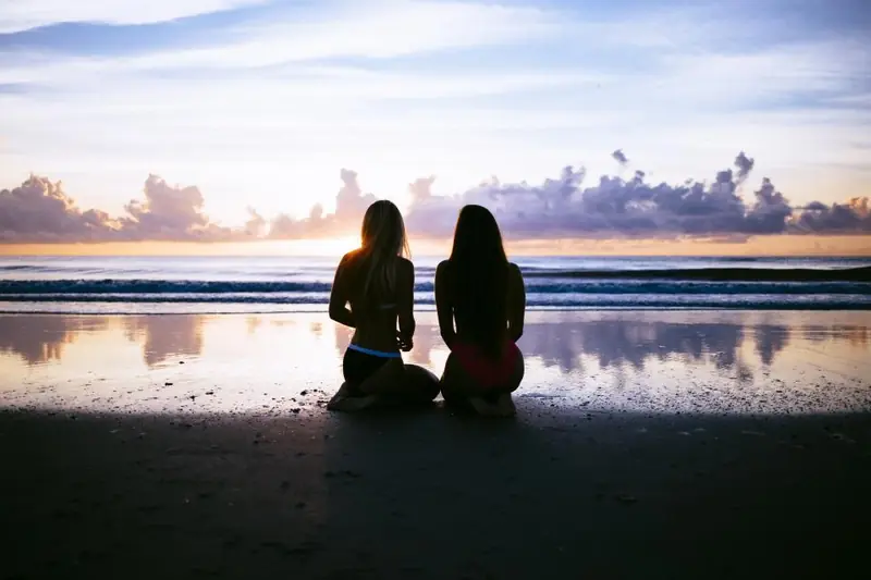 Deux femmes assises face à la mer au coucher du soleil
