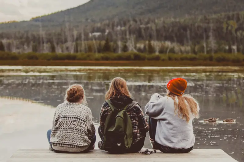 Trois amies assises sur un ponton au bord d’un lac