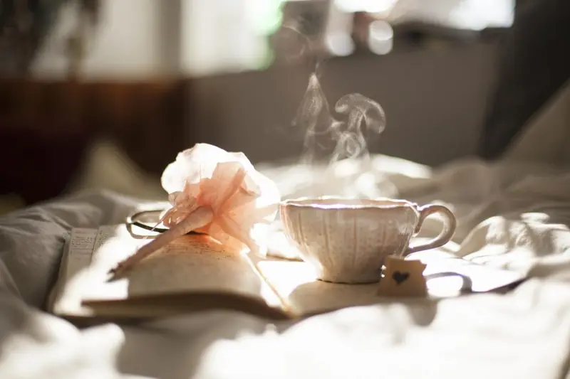 Tasse de thé fumante et livre ouvert sur un lit