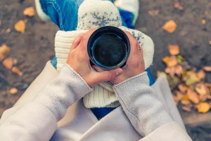 Mains en mitaines autour d’une boisson chaude, feuilles d’automne