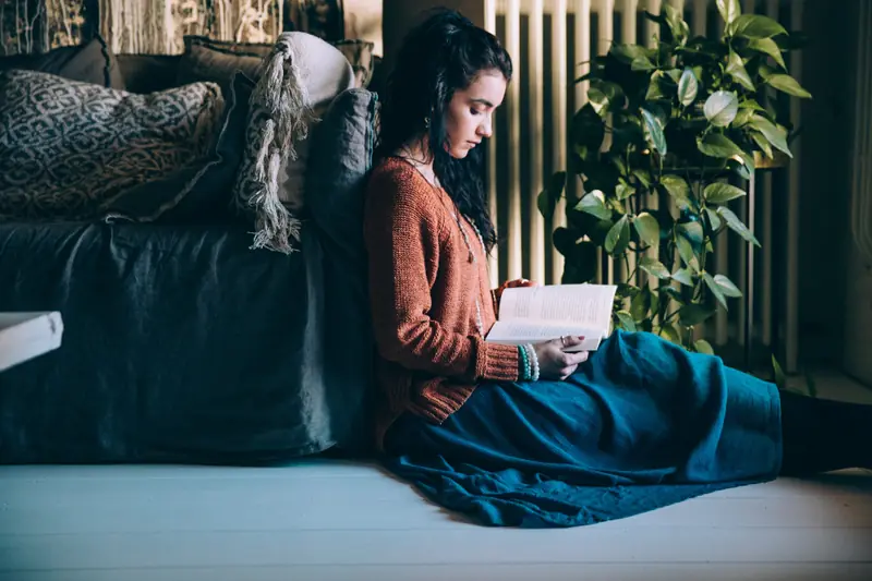 Femme lisant près d’une fenêtre, entourée de plantes