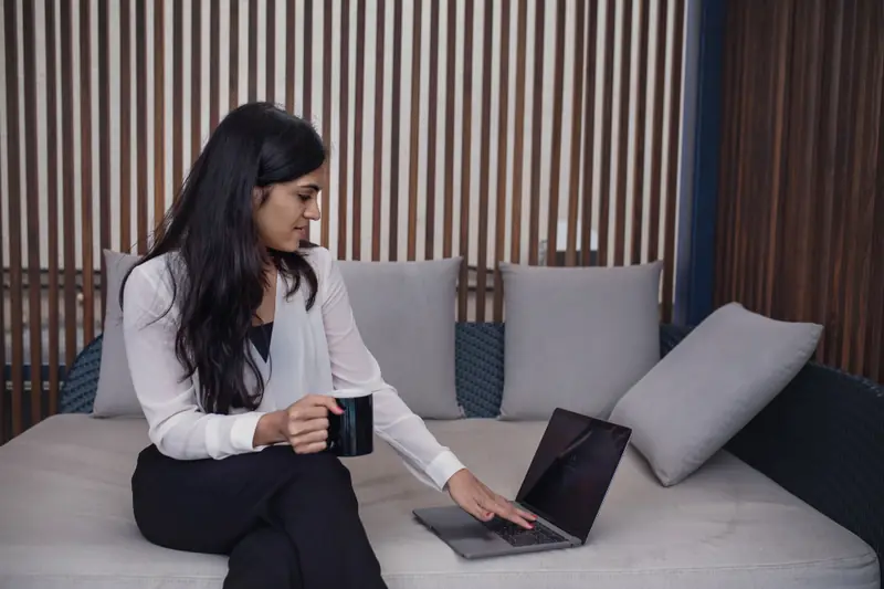 Femme avec son ordinateur et une tasse sur un canapé