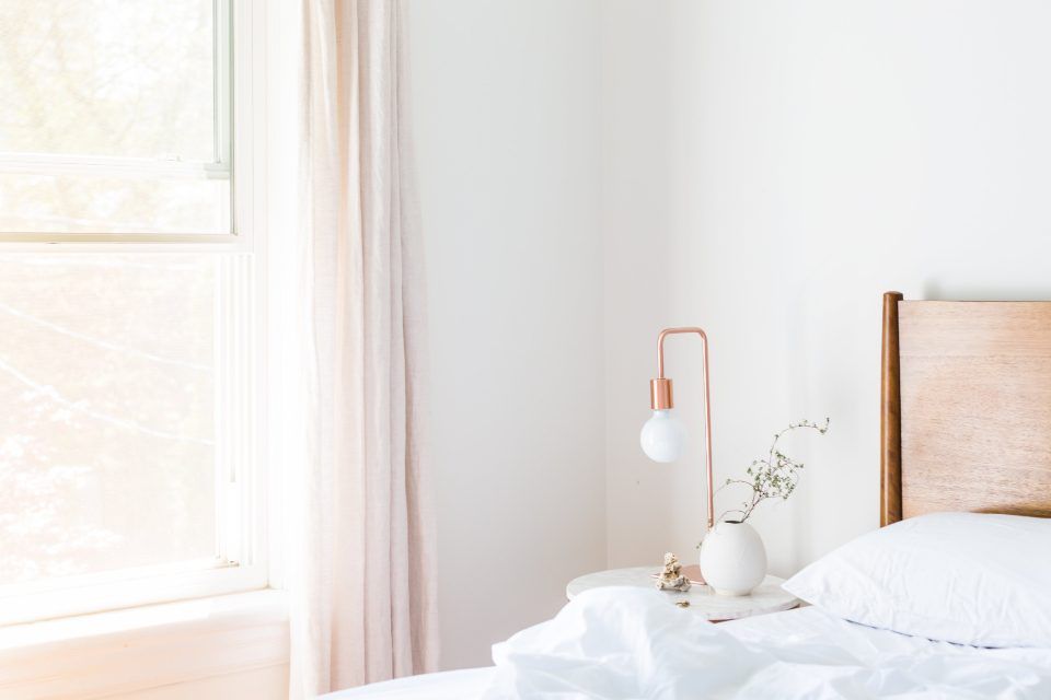 Chambre lumineuse le matin, lit aux draps blancs, lampe de chevet et grande fenêtre voilée